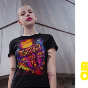 以下が含まれることがあります： 映画のポスターのカラフルなグラフィックプリントが施された黒いTシャツ。ポスターには、ネオンのようなフォントで「Enter the Void」というテキストが書かれています。