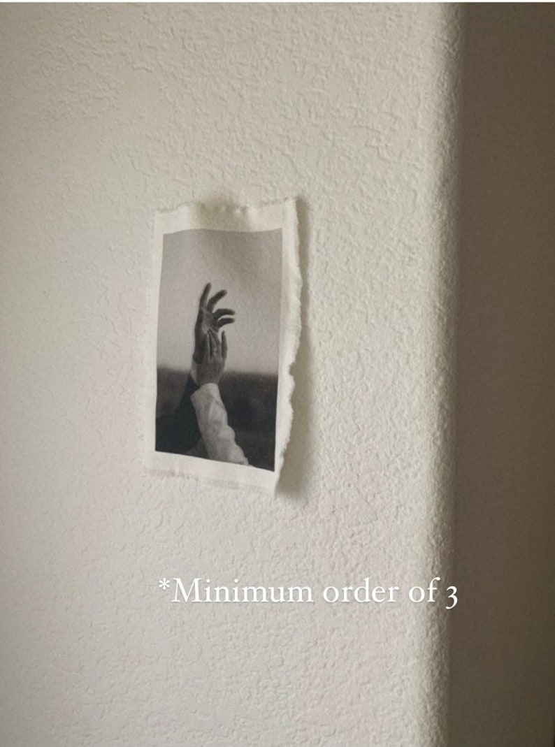 Puede incluir: Fotograf&iacute;a en blanco y negro de dos manos que se alzan hacia el cielo. La foto est&aacute; montada en una pared blanca con el texto "*Minimum order of 3" escrito debajo.
