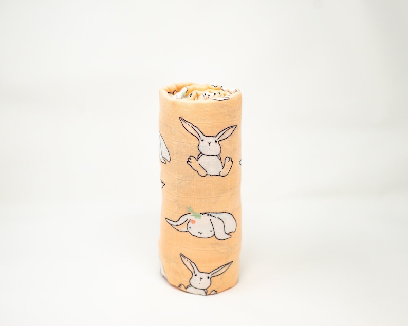 May include: A rolled up yellow muslin swaddle blanket with a white bunny rabbit print.