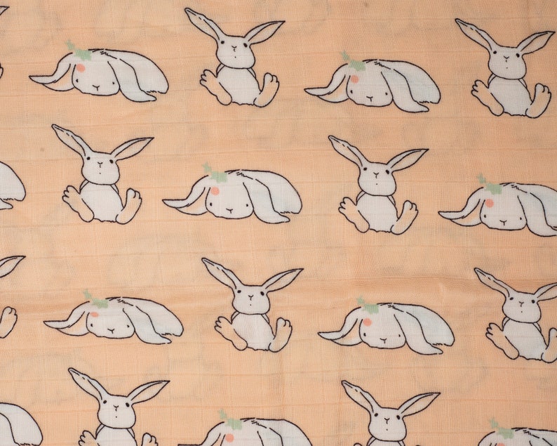 May include: A peach-colored fabric with a repeating pattern of white bunnies. The bunnies have small, green leaves on their heads and are in various poses.