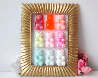 Puede incluir: Una obra de arte enmarcada en oro con coloridos caramelos de gominola con forma de oso. Los osos están dispuestos en filas de tres, con colores que incluyen rojo, naranja, rosa, amarillo y azul. El marco tiene un diseño texturizado y ornamentado.