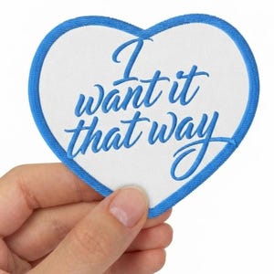 May include: A heart-shaped embroidered patch with a white background and a blue border. The text "I want it that way" is stitched in blue cursive script across the centre of the patch, creating a clear and legible design for fabric application.