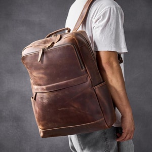 Puede incluir: Una mochila de cuero marrón con un bolsillo frontal con cremallera y correas ajustables.