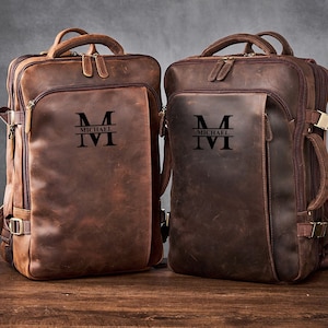 May include: Two brown leather backpacks with a personalized monogram. The monogram is a capital "M" with the name "Michael" written underneath.