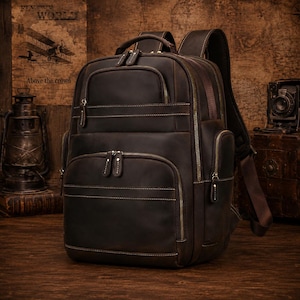 May include: A dark brown leather backpack with multiple zippered compartments and a top handle. The bag has visible stitching and a vintage aesthetic. The text "Above the crowd" is visible in the background.