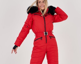 Könnte beinhalten: Ein roter Ski-Overall mit einer schwarzen, pelzbesetzten Kapuze und einem schwarzen Gürtel. Der Overall hat einen Reißverschluss vorne und Taschen an den Seiten. Das Model trägt eine schwarze Skibrille.