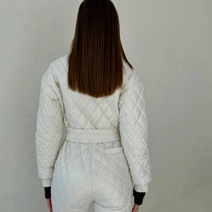 May include: A white quilted jumpsuit with a black elastic waistband and black trim on the cuffs. The jumpsuit has a diamond quilted pattern.