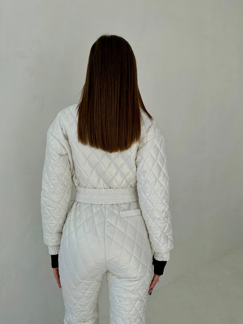 May include: A white quilted jumpsuit with a black elastic waistband and black trim on the cuffs. The jumpsuit has a diamond quilted pattern.
