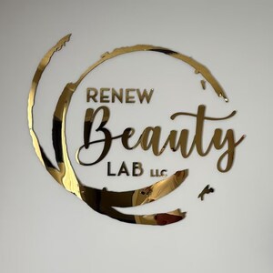 以下が含まれることがあります： 円形のデザインと「RENEW Beauty LAB LLC」というテキストが書かれた金色のロゴ