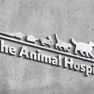 May include: A silver-toned metal sign featuring the text The Animal Hospital in a bold, sans-serif font. Above the text, a horizontal line supports a series of small, metallic animal silhouettes, including a lizard, turtle, rabbit, cat, dog, and bird.
