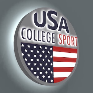 May include: A round, silver sign with the text "USA COLLEGE SPORT" in white lettering. The sign features a red, white, and blue American flag design.