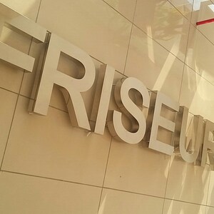 Puede incluir: Un letrero plateado con las palabras "FRISEUR SELCUK" en una pared de azulejos beige.