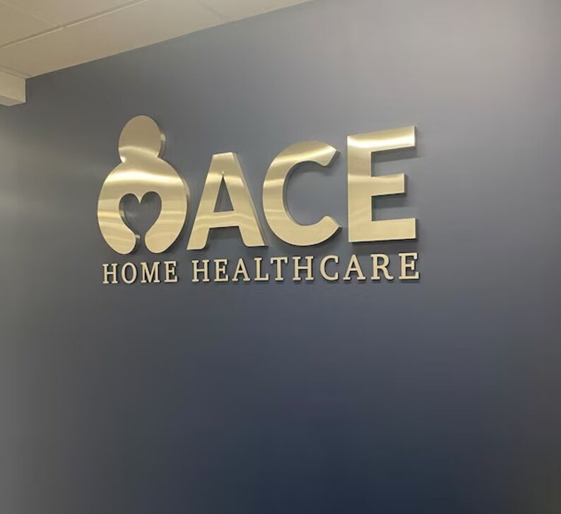 Puede incluir: Un letrero de metal dorado con la palabra "ACE" y la frase "HOME HEALTHCARE" en una pared gris.