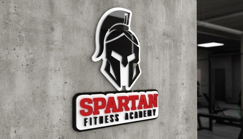 May include: A three-dimensional wall sign featuring a black Spartan helmet icon above a rectangular plaque with the red text SPARTAN and the black text FITNESS ACADEMY, all mounted on a textured gray concrete surface with a white border.