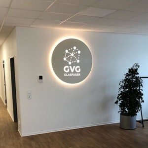 May include: A white circular sign with a glowing halo around the edge. The sign has a white logo with a network of connected dots and the text "GVG GLASFASER".