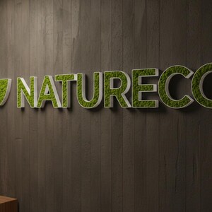 May include: A three-dimensional wall sign featuring the word NATURECO in white capital letters filled with green preserved moss, accompanied by a leaf-shaped logo icon also filled with green moss, mounted on a dark brown vertical wood panel.