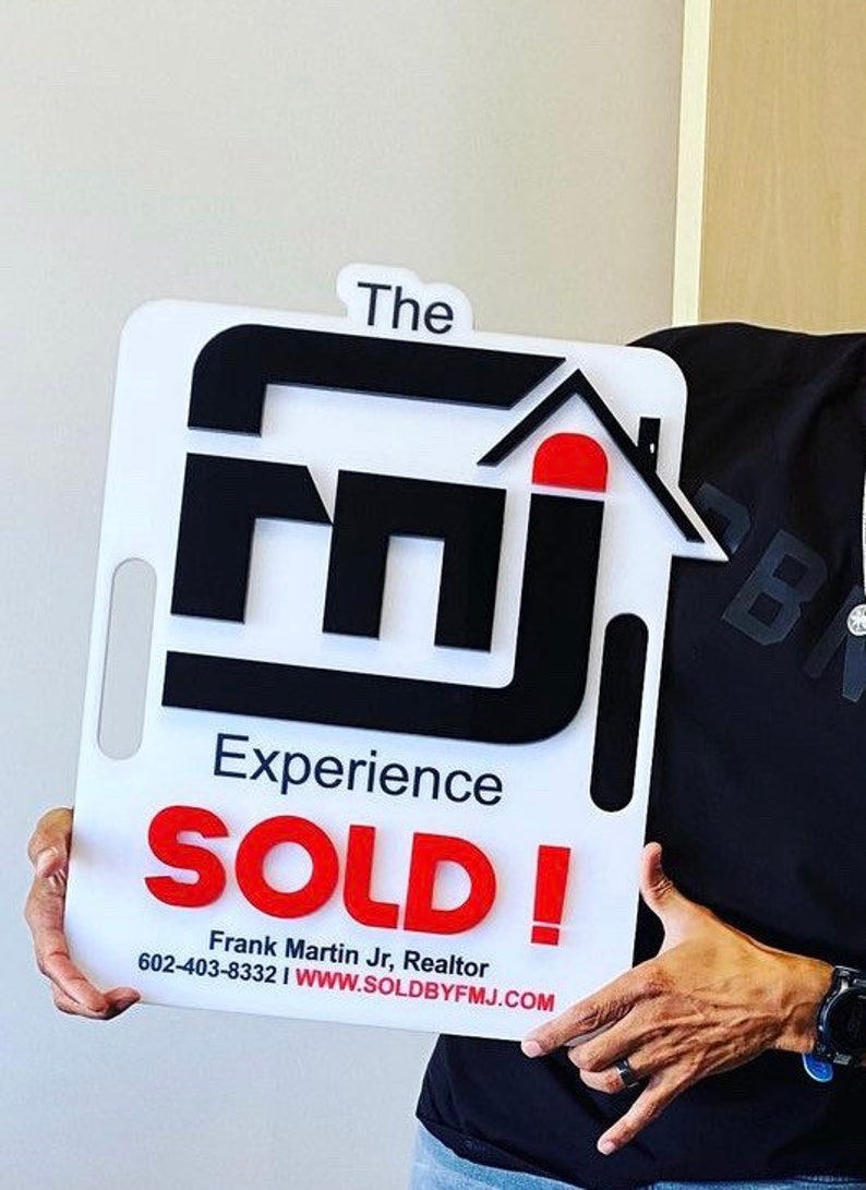 May include: A white rectangular sign with a handle cutout featuring the black text 'The' above a large black 'fmj' logo with a red roof icon. Below, the text reads 'Experience', 'SOLD!' in red, 'Frank Martin Jr, Realtor', and '602-403-8332 | WWW.SOLDBYFMJ.COM'.