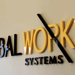 Könnte beinhalten: Ein dreidimensionales Wandschild mit dem Text GLOBAL WORKS SYSTEMS in einer Kombination aus schwarzen und gelben Buchstaben. Das Wort GLOBAL ist schwarz, WORKS ist gelb und SYSTEMS ist schwarz. Eine schwarze Diagonale durchkreuzt das Wort WORKS.
