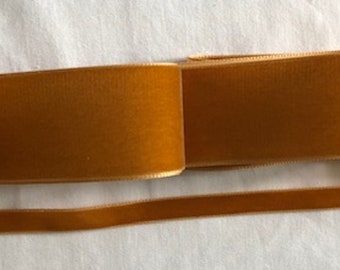 May include: A roll of brown velvet ribbon. The ribbon is folded in half and the ends are overlapping. The ribbon is on a white surface.