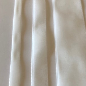 May include: Three white velvet ribbons of different widths. The ribbons are smooth and have a subtle sheen.