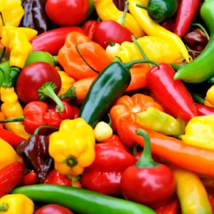 May include: A colourful selection of peppers in various shades of red, yellow, orange, and green. The image displays a mix of shapes and sizes, from small round cherry peppers to long, slender jalapeños. A fresh, natural food image.