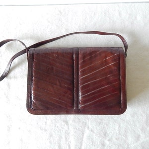 May include: A brown leather shoulder bag with a chevron pattern. The bag has a long strap and a flap closure.