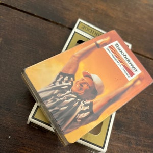 Puede incluir: Una baraja de cartas con un árbitro con una camisa a rayas en la parte delantera. La caja es amarilla y dice "Touchdown The Powerful Choice" en la parte delantera.