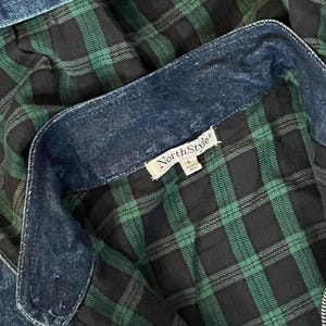 May include: Close-up of a denim jacket with a green and black plaid lining. The jacket has a zipper and a collar. The tag reads "NorthStyle". The denim is a medium wash blue.