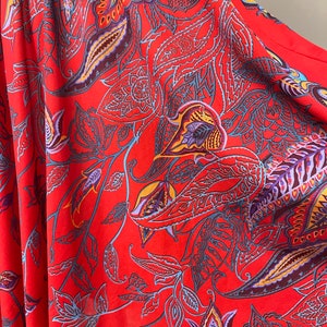 May include: Red fabric with a paisley pattern. The pattern features intricate floral designs in shades of blue, purple, yellow, and orange.
