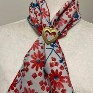 May include: A white silk scarf with a red floral pattern and a gold heart-shaped brooch.
