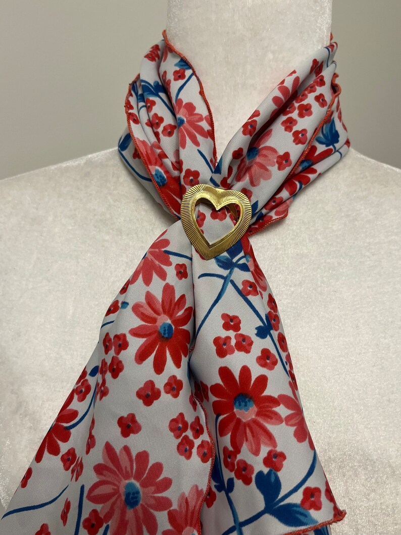 May include: A white silk scarf with a red floral pattern and a gold heart-shaped brooch.