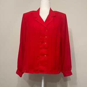 May include: A red long-sleeved blouse with a collared neckline and a double-breasted button closure.