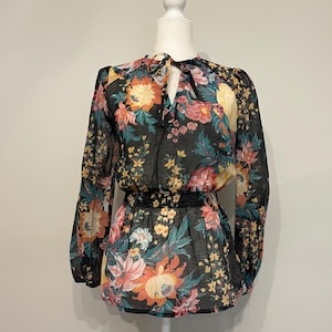 May include: Black floral print blouse with long sleeves and a tie-neck detail. The blouse features a fitted waist and a vibrant pattern of pink, orange, yellow, and teal flowers. The sheer fabric adds a delicate touch to the design.