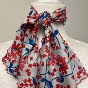 May include: A white scarf with a red and blue floral pattern. The scarf has a scalloped edge and is tied in a bow around a white mannequin.