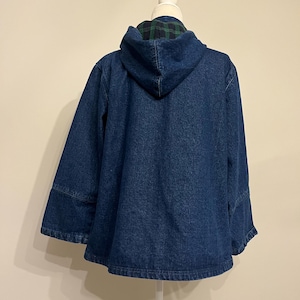 May include: A dark blue denim jacket with a hood. The hood lining features a green and black plaid pattern. The jacket has a relaxed fit and wide sleeves, displayed on a white mannequin.