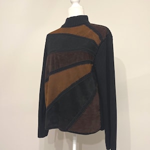 May include: A black, brown, and tan patchwork sweater with a mock turtleneck. The sweater has long black sleeves and a ribbed knit collar. The front of the sweater features a geometric design with suede-like patches.