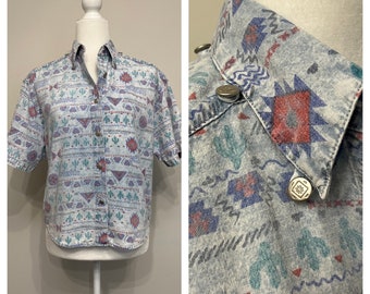 May include: A short-sleeved, light blue button-down shirt with a geometric pattern in shades of blue, red, and green. The shirt has a pointed collar and a button-up front.