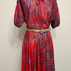 May include: A red midi dress with a paisley print and a gold belt. The dress has a V-neckline and short sleeves.