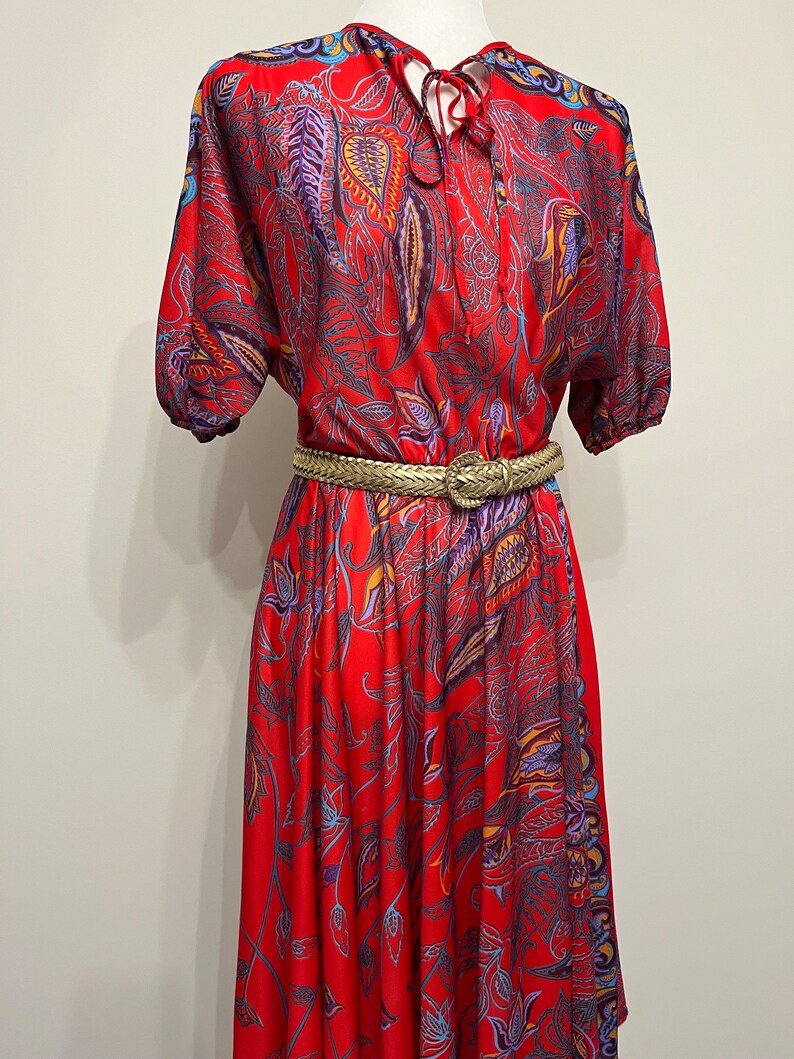 May include: A red midi dress with a paisley print and a gold belt. The dress has a V-neckline and short sleeves.