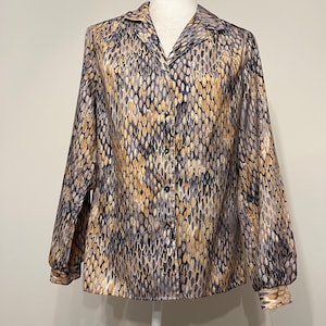 May include: A button-down blouse with a unique pattern. The long-sleeved shirt features a repeating design in shades of gold, gray, and black. The blouse has a collared neckline and button closures down the front. The sleeves have buttoned cuffs.