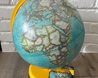 May include: A yellow globe with a blue and brown map of the world. The globe is on a yellow stand and has a small booklet that says "National Geographic Using Your Globe".