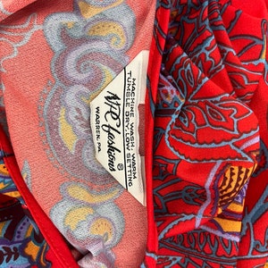 May include: A red fabric with a paisley pattern. The fabric has a white tag with the text "NFC Fashions" and "WARREN, PA.". The tag also includes instructions for washing and drying the fabric.