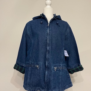 May include: A dark blue denim jacket with a hood and a zipper closure. The jacket has two front pockets with zippers and green and black plaid cuffs. The jacket is displayed on a white mannequin.