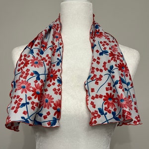 May include: A white scarf with a red and blue floral pattern. The scarf has a scalloped edge and is displayed on a white mannequin.