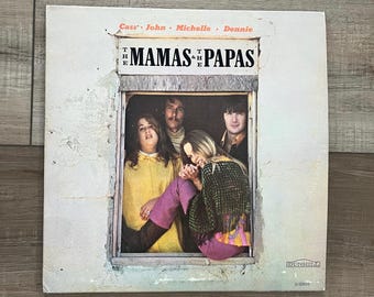Peut inclure: Pochette d'album vinyle vintage pour The Mamas & the Papas. La pochette de l'album présente une photographie des membres du groupe dans un cadre de fenêtre. Le titre de l'album est imprimé en lettres noires. La pochette de l'album est sur une surface en bois.