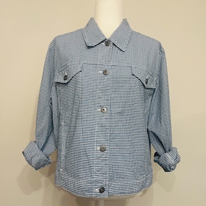 May include: A blue and white gingham jacket with a collared neckline, two chest pockets, and button closures. The sleeves are rolled up, revealing the gingham pattern. The jacket is displayed on a mannequin.