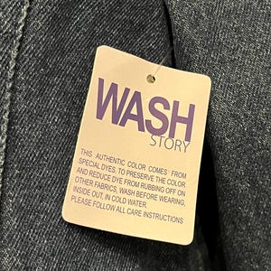 May include: Close-up of a denim garment with a tag that reads "WASH STORY" in purple text. The tag provides care instructions, including washing in cold water and washing inside out.