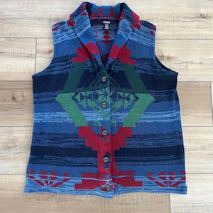May include: A blue, red, green, and black patterned knit vest with a shawl collar and button closure. The vest has the word "Chaps" on the label.