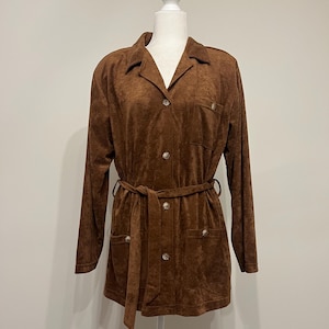 May include: A brown suede jacket with a button-up front, long sleeves, and a belt. The jacket has two pockets on the front and a collar.