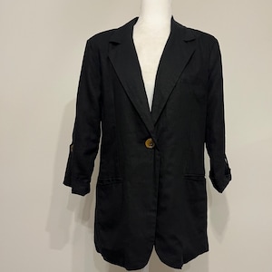 May include: A black blazer with a single button closure and two front pockets. The blazer has three-quarter sleeves and is displayed on a white mannequin. The blazer is made of a lightweight fabric.